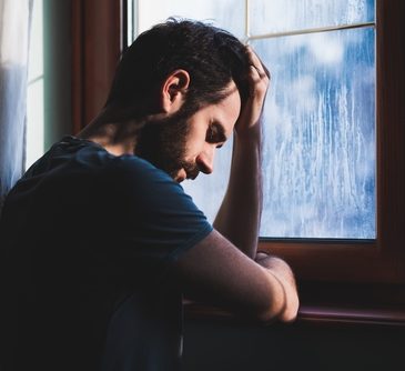 A man at a window holding his head in his hand