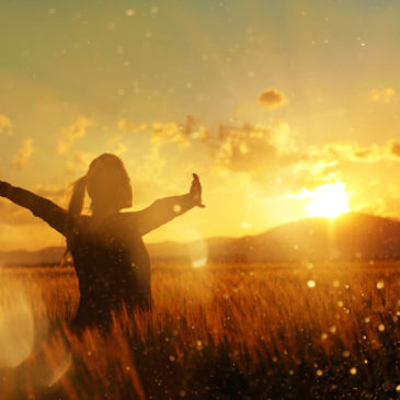 silhouette in the sunset, young woman with her arms raised enjoying summer twilight in the middle of nature.