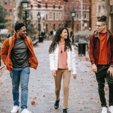 positive young students walking along pathway in city