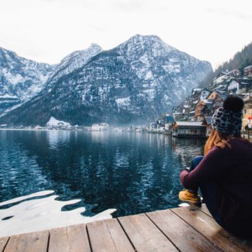 woman in purple sweater sitting on wooden floor with view of lake and mountains